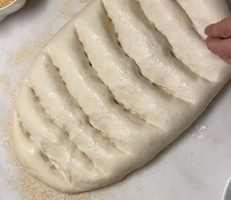 Rezept für Ramazan-Pide – Befeuchten Sie Ihre Hände gut, bevor Sie den Teig einritzen, da dieser sehr klebrig ist. Ritzen Sie den Teig mit einzelnen, gleichmäßigen Bewegungen ein und formen Sie dabei zunächst ein horizontales und anschließend ein schräges Muster, um das Baklava-Muster zu erzielen.